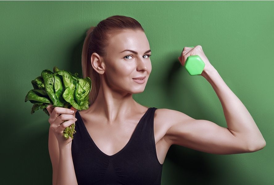 אישה ספורטיבית מחזיקה תרד ביד אחת ומשקולת בשנייה - מזון עם ברזל