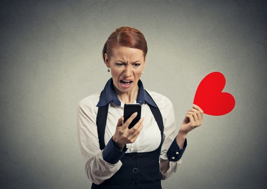 אישה מבוהלת אוחזת בלב וטלפון נייד - אפליקציית היכרויות