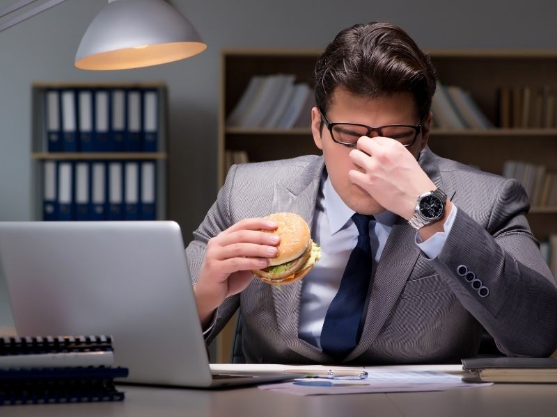 גבר אוכל המבורגר מול המחשב - אכילה רגשית להורדת לחץ