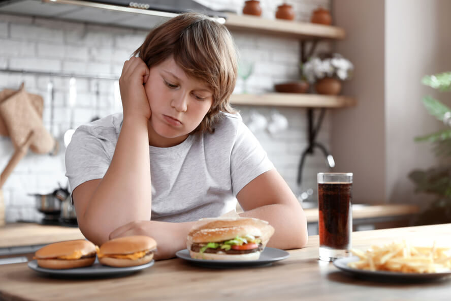 אכילה רגשית - ילד עצוב יושב במטבח ומביט בהמבורגרים