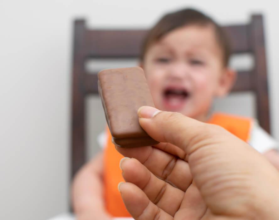 יד של אימא מציעה חטיף שוקולד לילד בוכה
