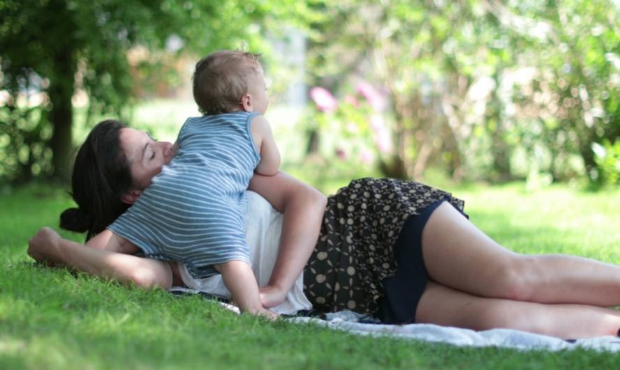אישה שוכבת בפארק על מדשאה ולצדה תינוק
