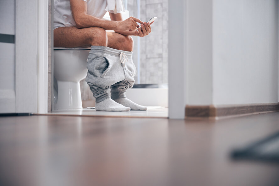 גבר יושב על אסלה עושה קקי בשירותים