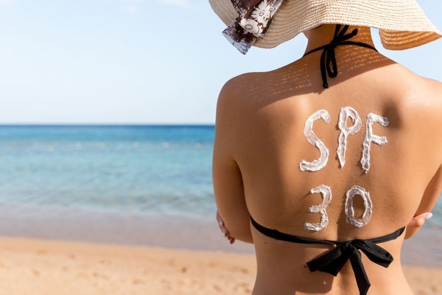גב של אישה בביקיני בחוף הים, עם כיתוב SPF 30 שנכתב עם קרם הגנה
