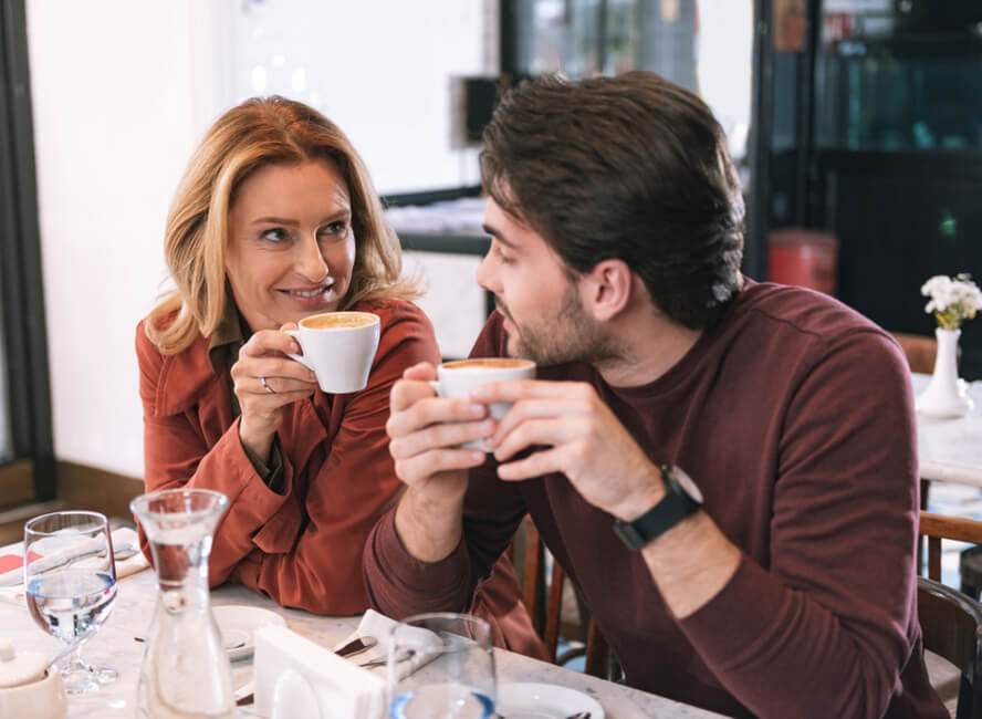 אישה בוגרת וגבר צעיר שותים קפה - זוגיות עם הפרש גילים
