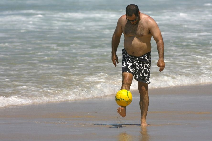 גבר עם כרס משחק בכדור בחוף הים - גבר בגיל המעבר