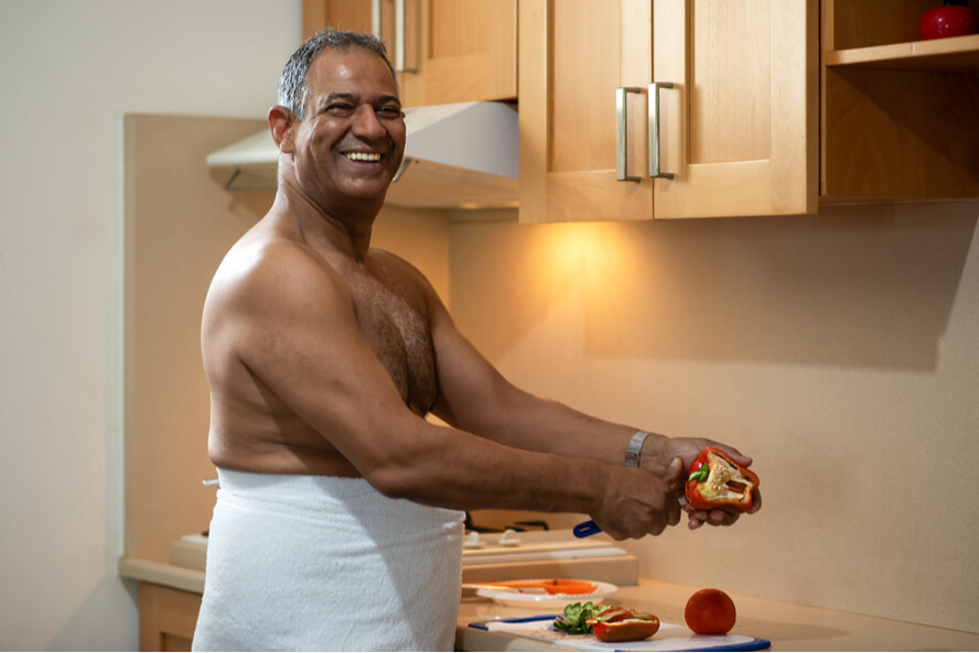 גבר מבוגר מחייך וחותך ירקות במטבח