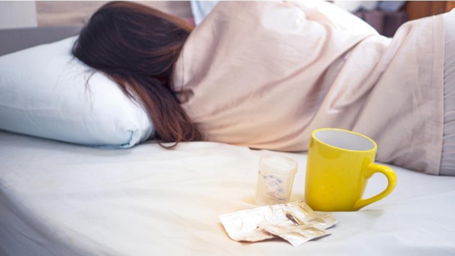 אישה שוכבת במיטה לצד ספל ותרופות - קלקול קיבה