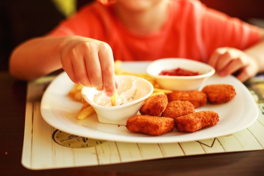 ילד אוכל נאגטס תעשייתי במסעדת מזון מהיר